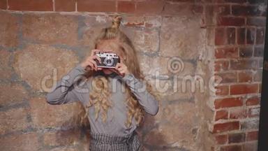 嬉皮士女孩在砖墙背景上的老式相机上摄影。 年轻女孩用复古相机拍照
